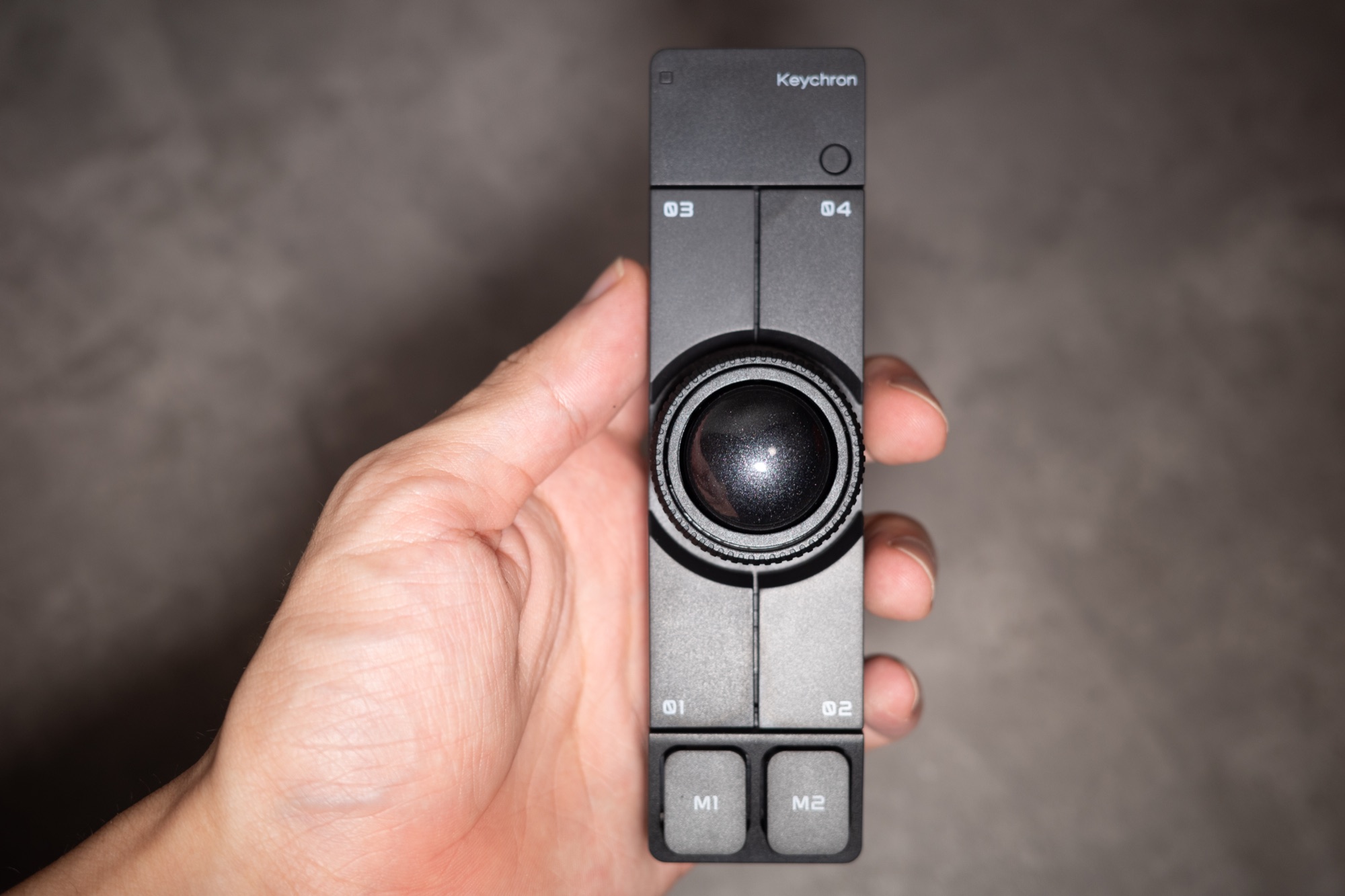 Keychron Nape Pro を手に持った正面。ボールの上下に 01〜04 の 4 ボタン、下端に M1・M2 が並ぶ